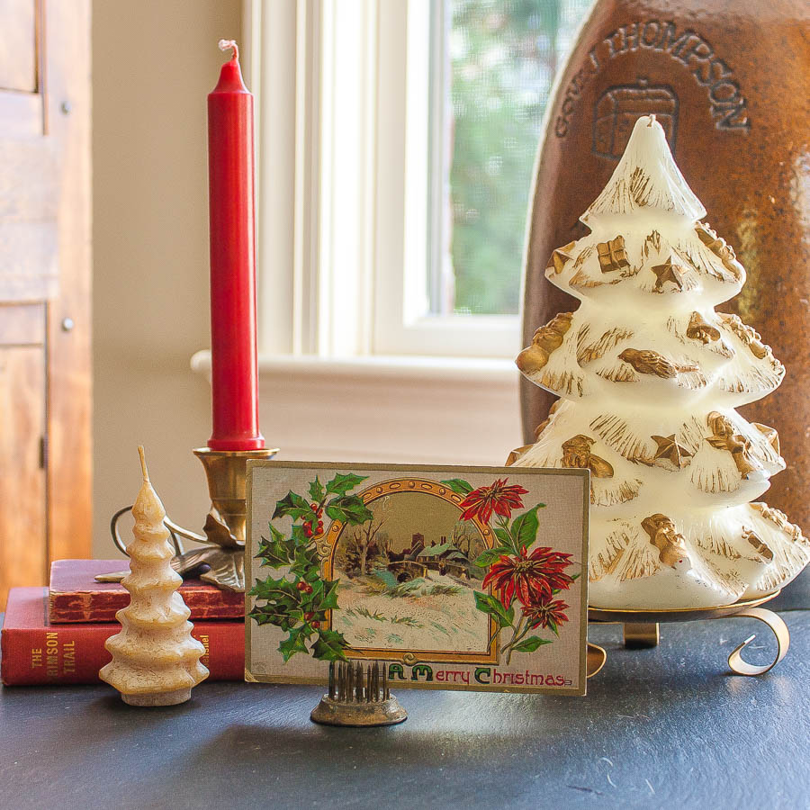 Christmas vignette with an early 1900's postcard, vintage Christmas tree candles, a vintage brass holly candle holder, a 1912 edition of The Crimson Trail by Elmer U. Hoenshel, and a 1903 edition of Ropp's New Calculator.