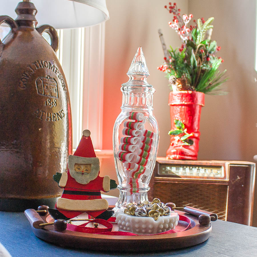 Christmas vignette with an antique Santa boot, vintage candy jar, 1970 Santa ornament, and a hobnob milk glass candy dish filled with jingle bells.