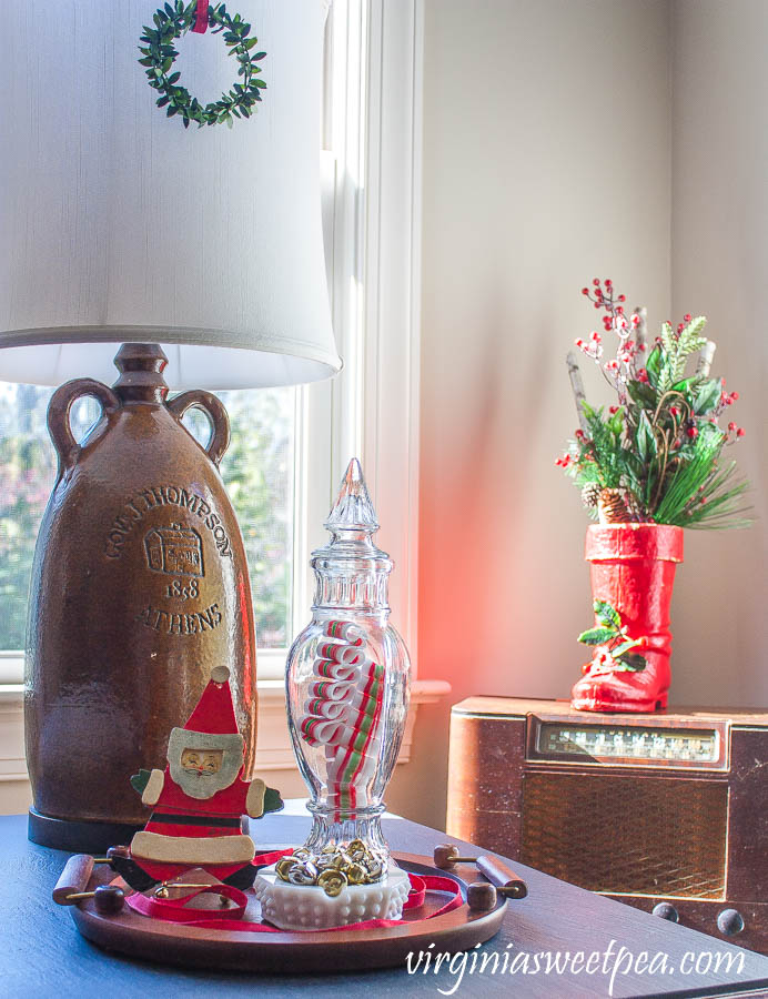 Christmas vignette with an antique Santa boot, vintage candy jar, 1970 Santa ornament, and a hobnob milk glass candy dish filled with jingle bells.