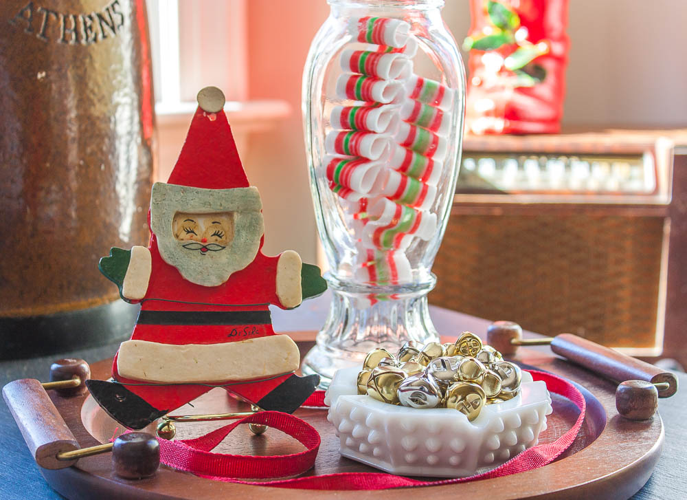 Christmas vignette with an antique Santa boot, vintage candy jar, 1970 Santa ornament, and a hobnob milk glass candy dish filled with jingle bells.