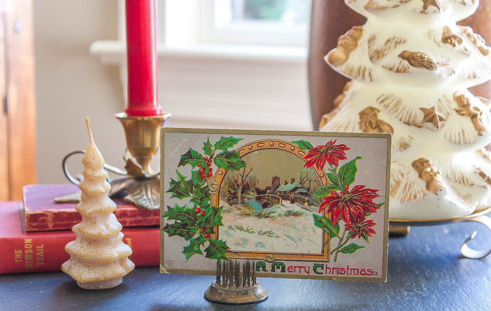 Christmas vignette with an early 1900's postcard, vintage Christmas tree candles, a vintage brass holly candle holder, a 1912 edition of The Crimson Trail by Elmer U. Hoenshel, and a 1903 edition of Ropp's New Calculator.