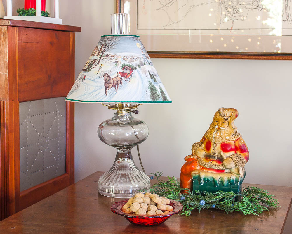 Antique lamp with a Christmas lamp shade with holes that illuminate the scene on it, vintage Santa bank, and a reindeer bowl filled with dog treats