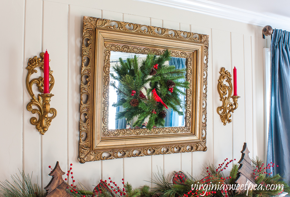 Gold mirror with a Christmas wreath flanked by vintage candle holders with red candles.