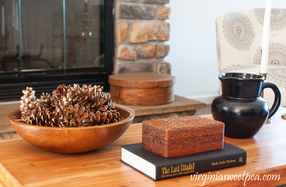 Winter coffee table decor with wood bowl filled with pine cones, carved wood box, black pitcher