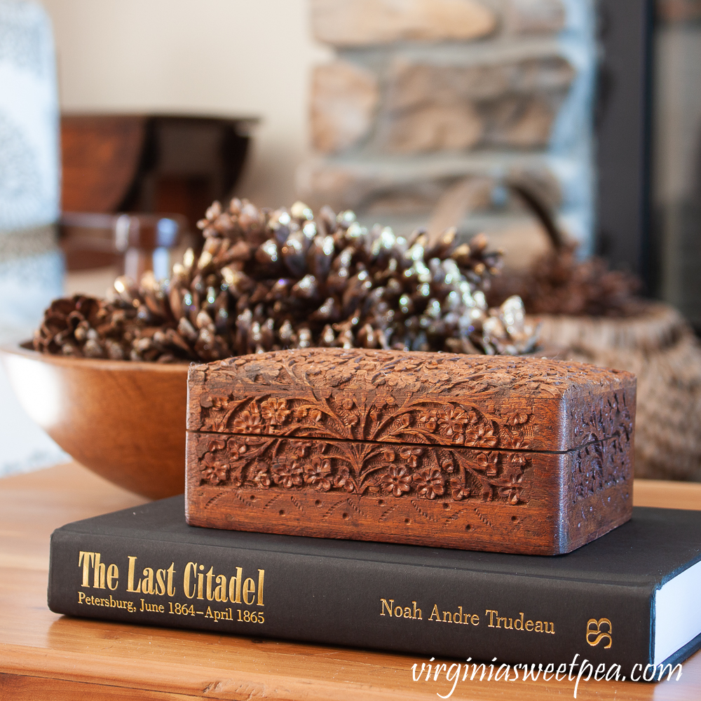 Winter coffee table decor with wood bowl filled with pine cones, carved wood box, and The Last Citadel book