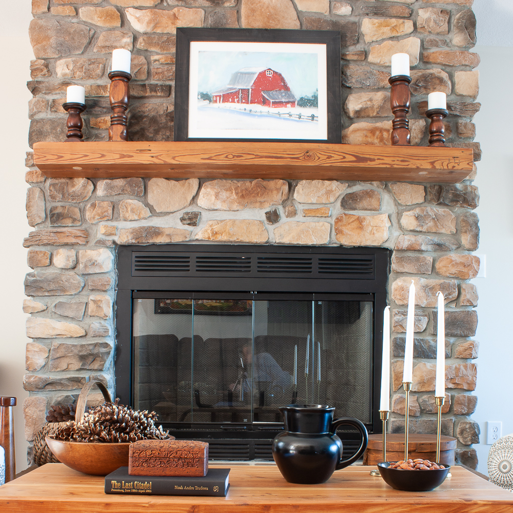 Rock fireplace with barn painting, wood candle holders, coffee table decorated for winter