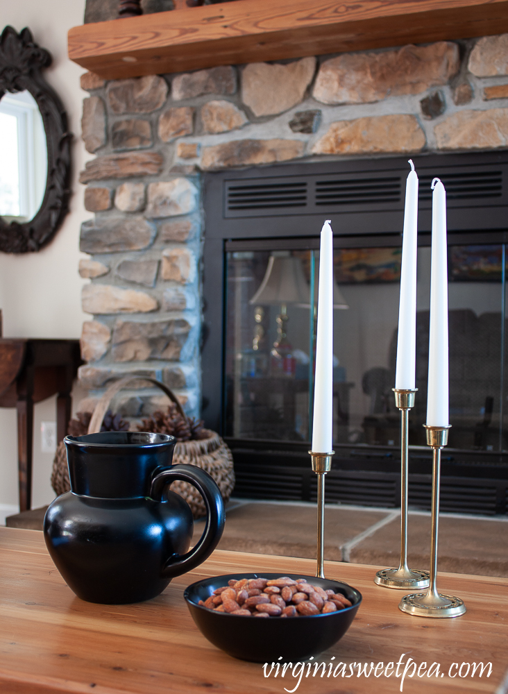 Vignette with black pitcher, black bowl filled with almonds, and three brass candlesticks with white candles