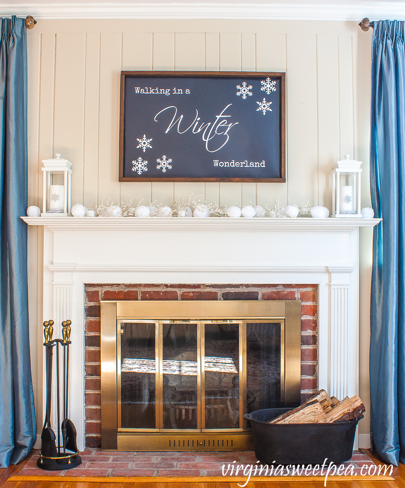 Mantel styled for winter with a "Walking in a Winter Wonderland" sign, white lanterns and snowballs.