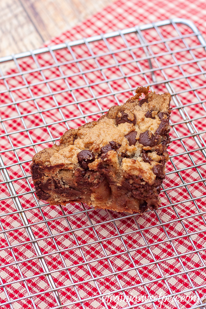 Piece of chocolate chip cookie cake on a wire rack with a red plaid napkin underneath