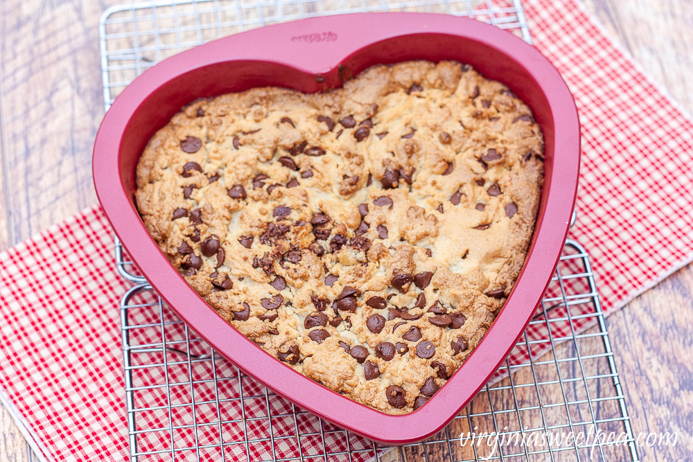 Chocolate chip cookie cake in a heart shaped pan on a wire rack with a red plaid napkin underneath