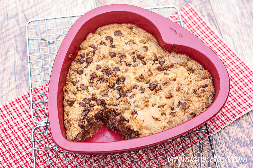 Chocolate chip cookie cake in a heart shaped pan on a wire rack with a red plaid napkin underneath