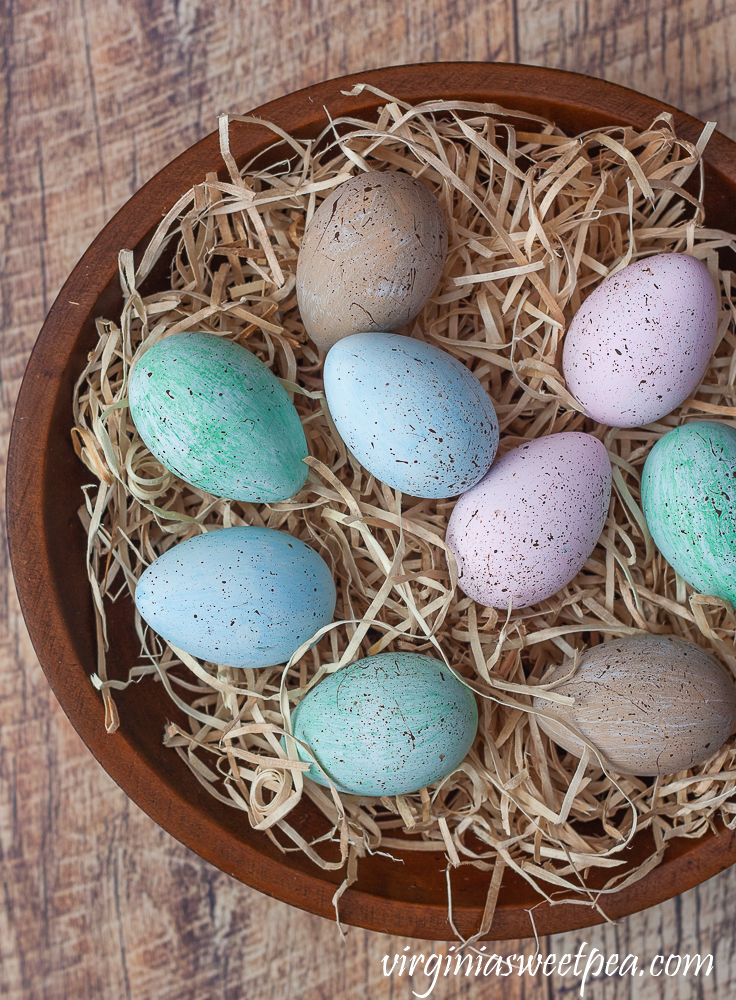 Speckled blue, green, and pink eggs in a wooden bowl filled with excelsior