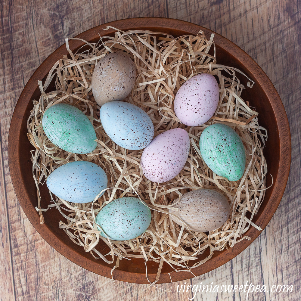 Speckled blue, green, and pink eggs in a wooden bowl filled with excelsior