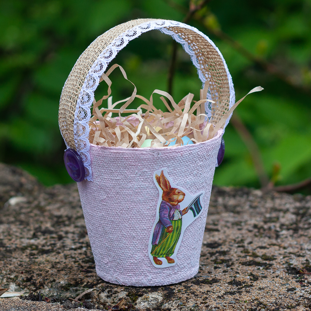 Easter treat basket made using a peat pot, ribbon, buttons, and an Easter sticker