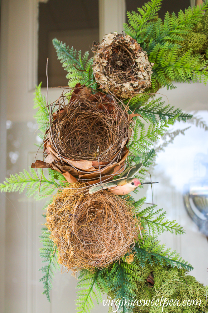 Three natural birds nests on a wreath with faux ferns and a faux hummingbird