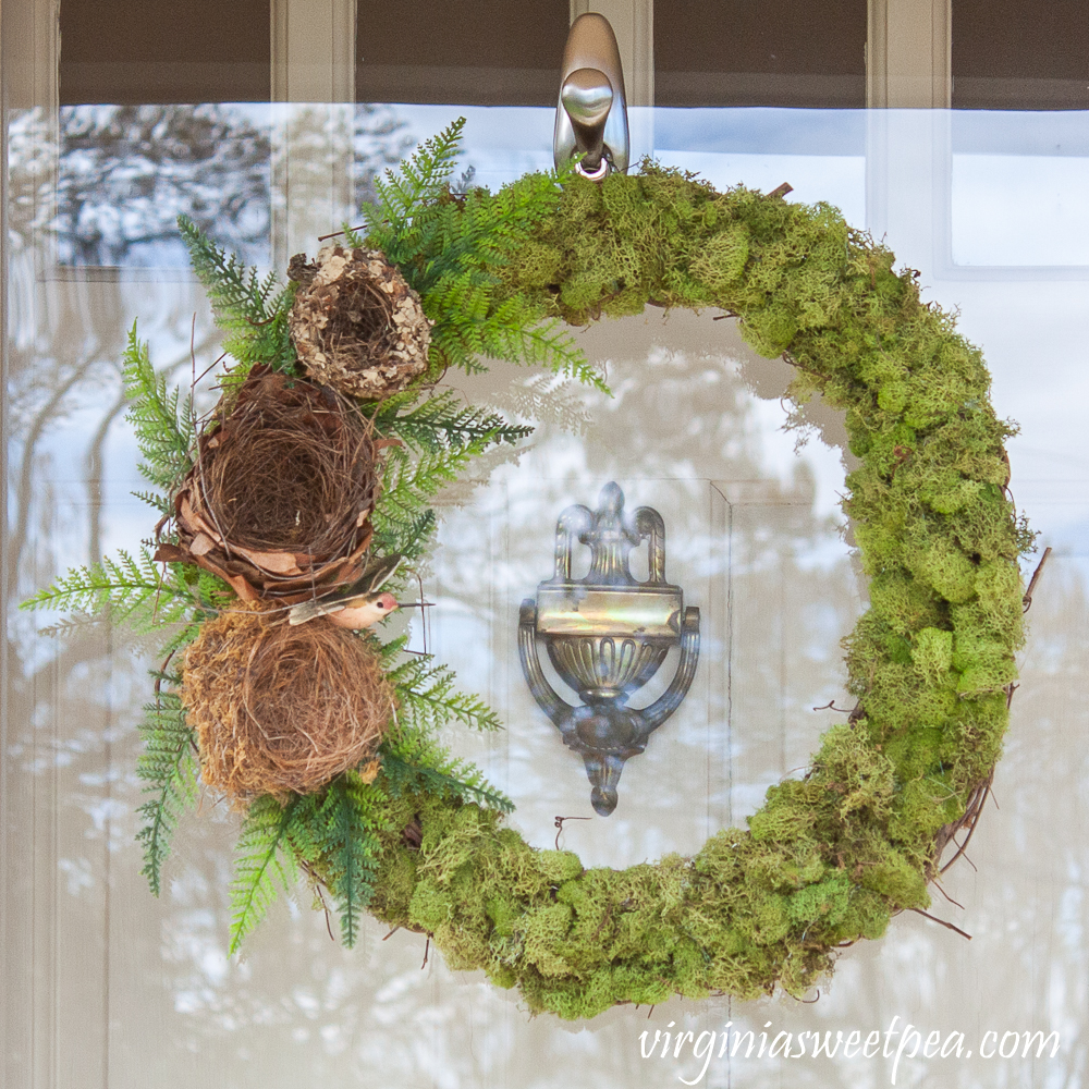 Wreath covered in moss with three nests, ferns, and a hummingbird on the side.