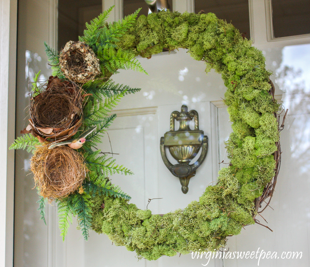 Wreath covered in moss with three nests, ferns, and a hummingbird on the side.