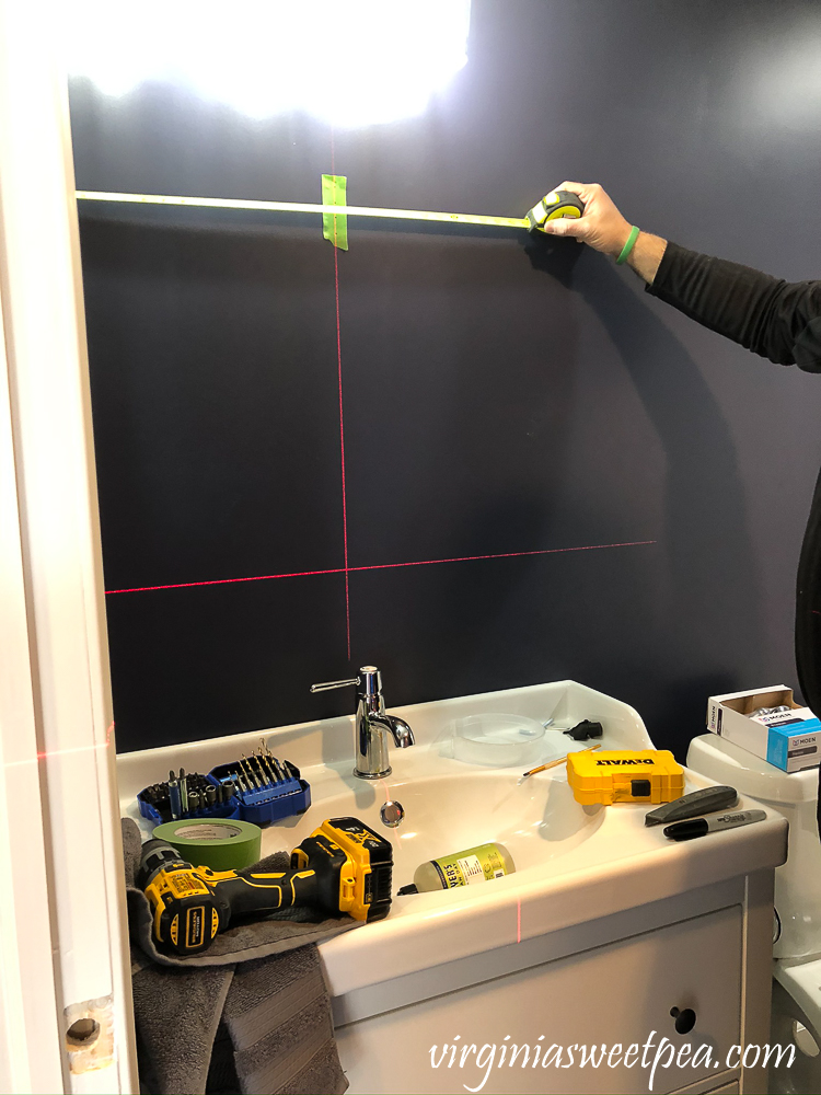 Using a laser level to help install a mirror in a bathroom.