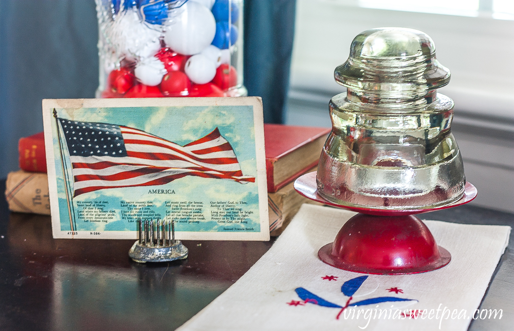 Vintage American flag postcard with a glass insulator on top of a red candle holder on a vintage towel