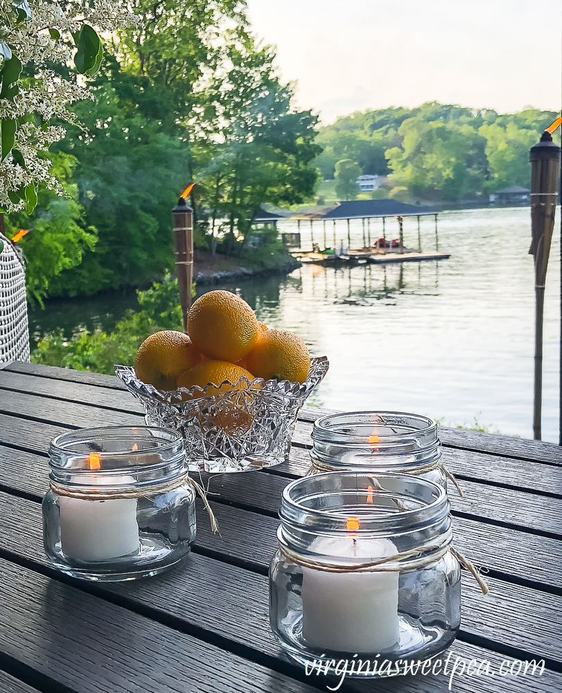 Citronella candles in Mason jars with a bowl of lemons all with a lake view