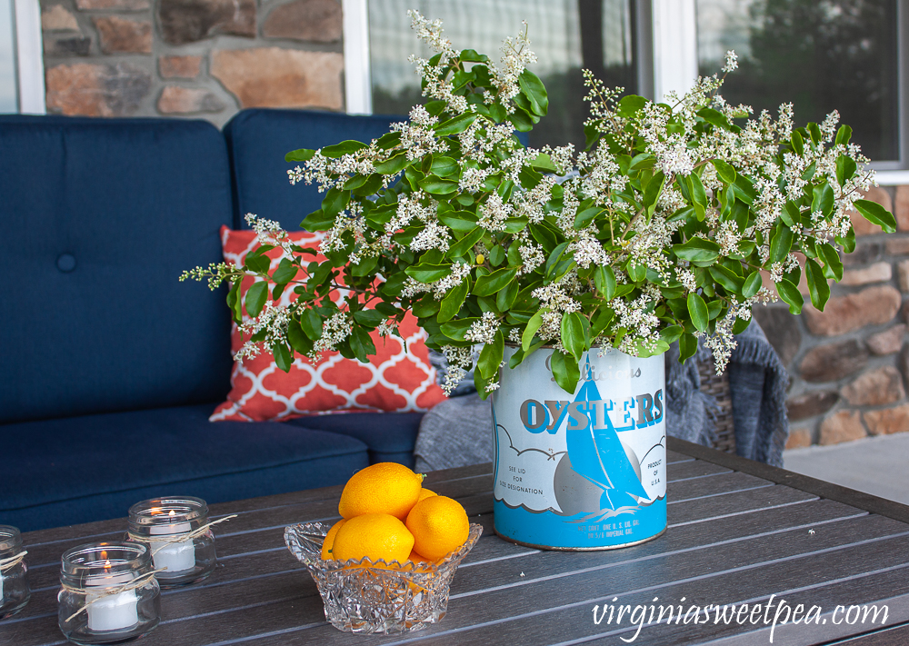 Flowers on a patio in a vintage oyster can with candles and a bowl of lemons