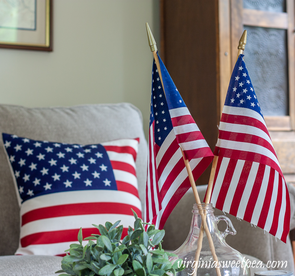 American flags displayed in a clear glass vintage jug with an American flag pillow