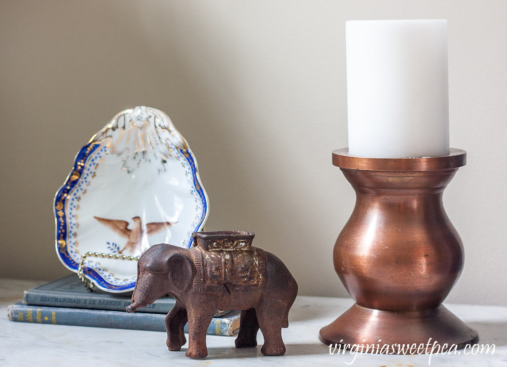 Vignette with an eagle dish, elephant, vintage books, and a copper candle holder with a white candle.