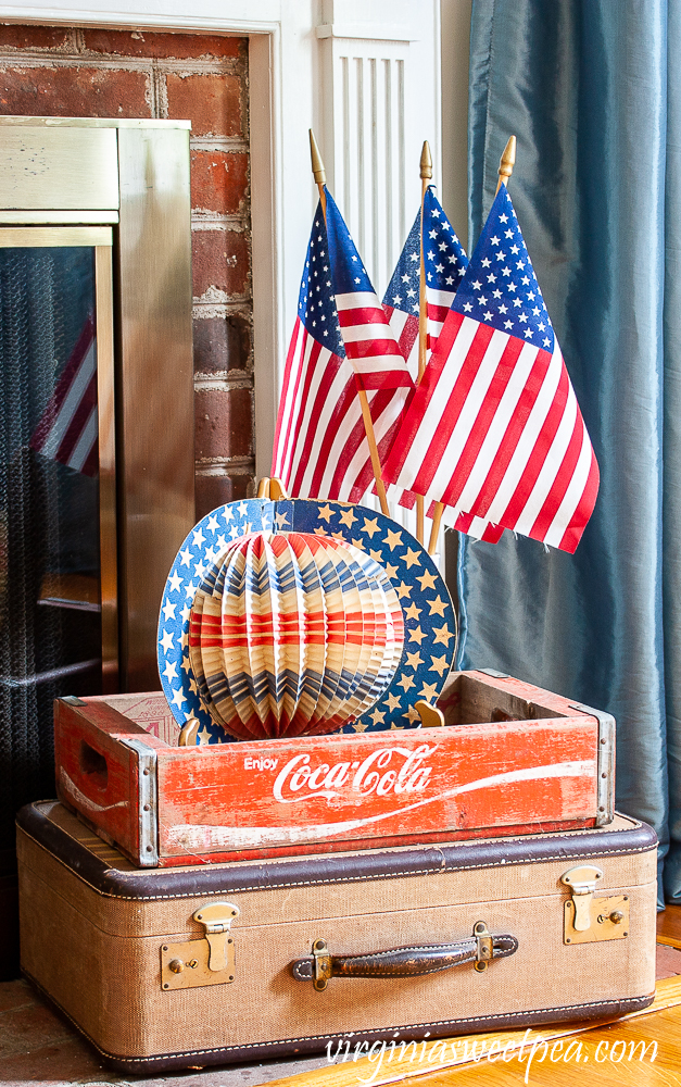 Patriotic Display with vintage suitcase, Coca-Cola crate, American flags, and a vintage red, white, and blue hat.