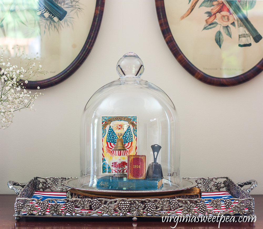 Cloche on a silver tray decorated with a Liberty Bell postcard, 1924 mini book, a vintage bell, and a vintage bible.