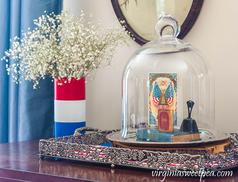 Patriotic Vignette with a red, white and blue striped vase with Baby's Breath and a cloche with a Liberty Bell postcard, 1924 mini book, a vintage bell, and a vintage bible.