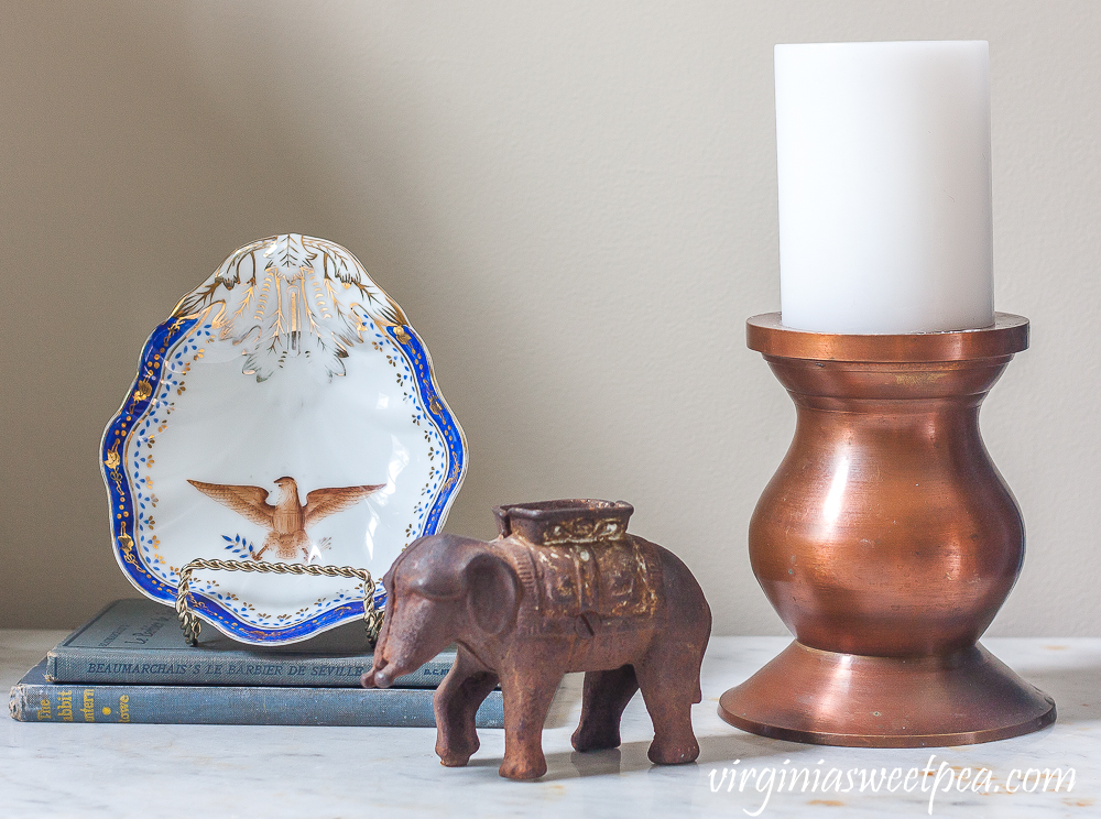 Vignette with an eagle dish, elephant, vintage books, and a copper candle holder with a white candle.