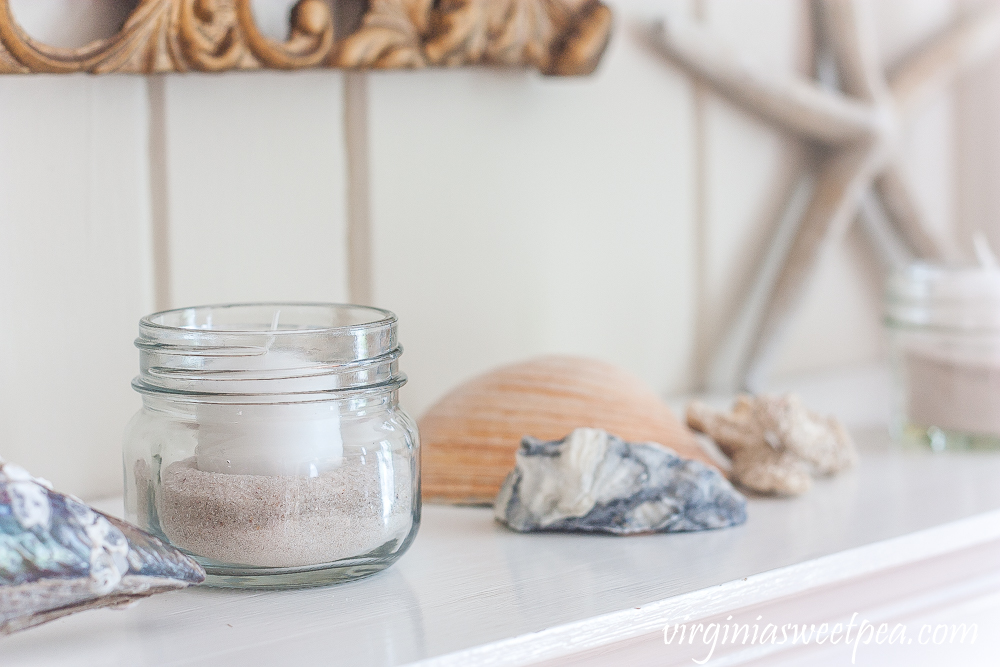 Summer mantel with shells, starfish, and small jars filled with sand and white votive candles.