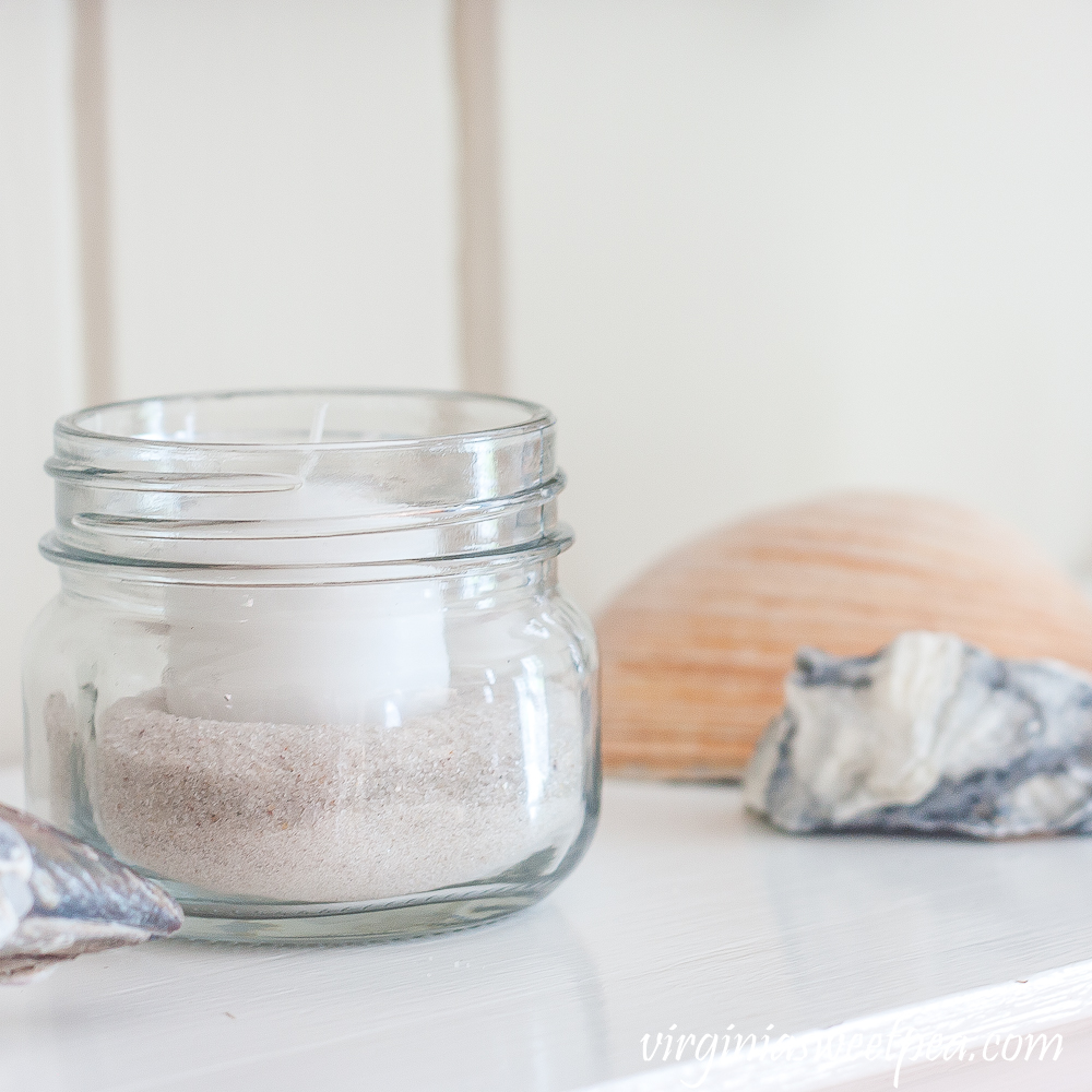 Summer mantel with a jar filled with sand and a votive candle with a clam shell and an oyster shell in the background.