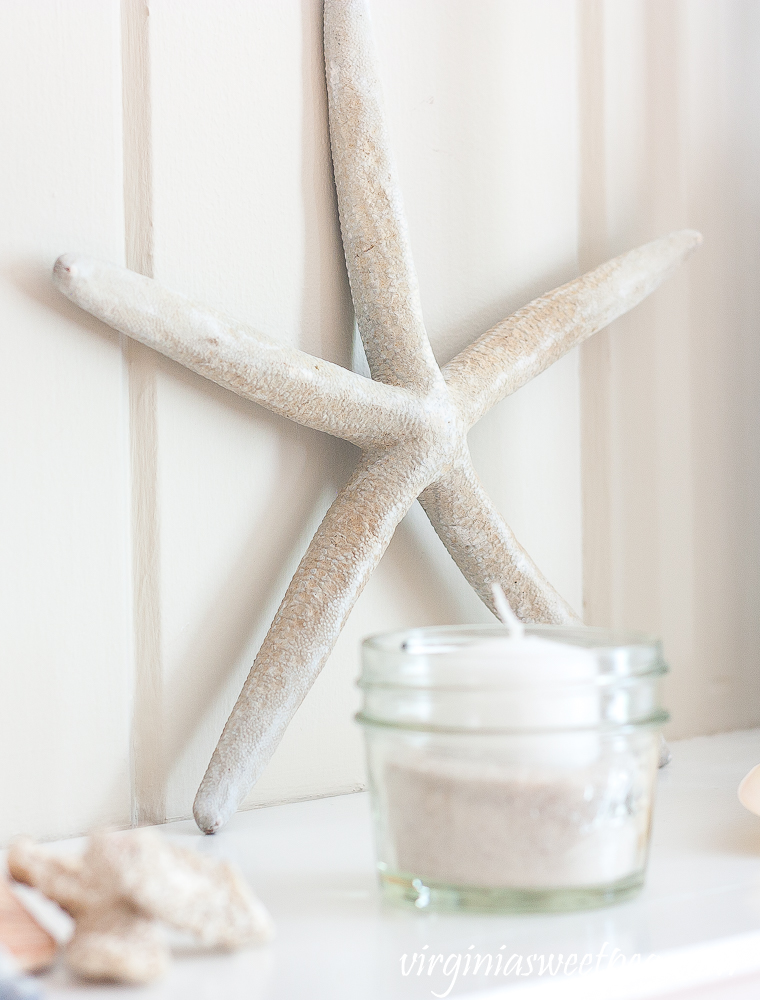 Starfish leaning against a mantel with a Ball jar filled with sand and a white votive candle.