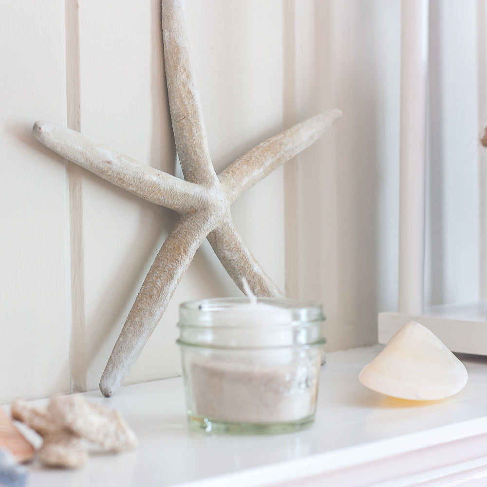 Starfish leaning against a mantel with a Ball jar filled with sand and a white votive candle.