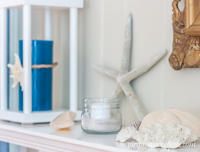 Summer mantel with starfish, shells, sand dollar, coral, and a lantern holding a blue candle.