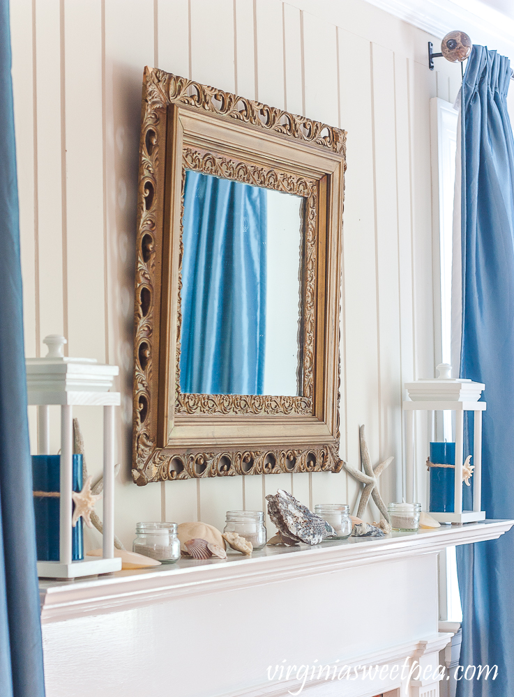 Gold mirror over a mantel decorated with a coastal theme.