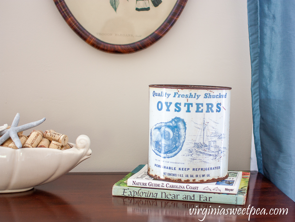 vintage oyster tin on top of two books with McCoy planter filled with wine corks and starfish