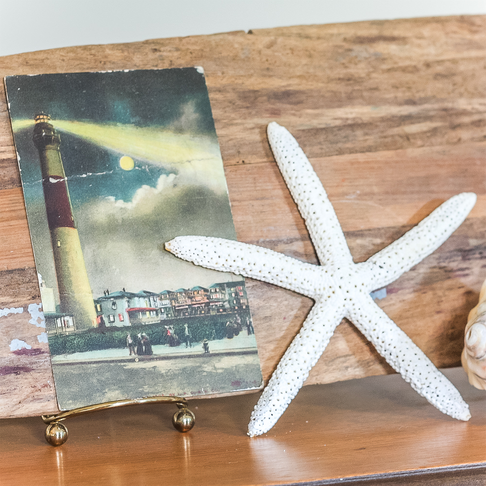 Vintage 1907 postcard with a lighthouse displayed with a starfish with a vintage oar in the background.