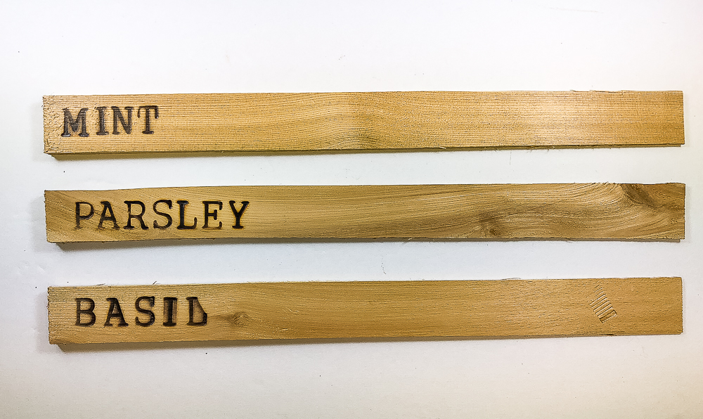 Plant markers made by wood burning plant names on wood shims.