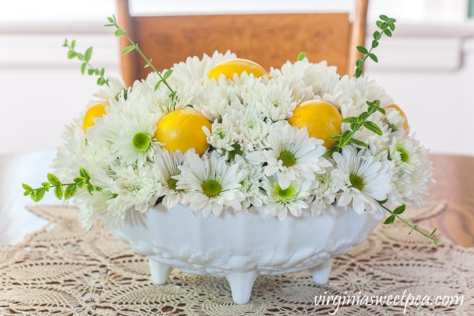 Flower arrangement with Chrysanthemums, and Lemon in a white Indiana milk glass footed fruit bowl.