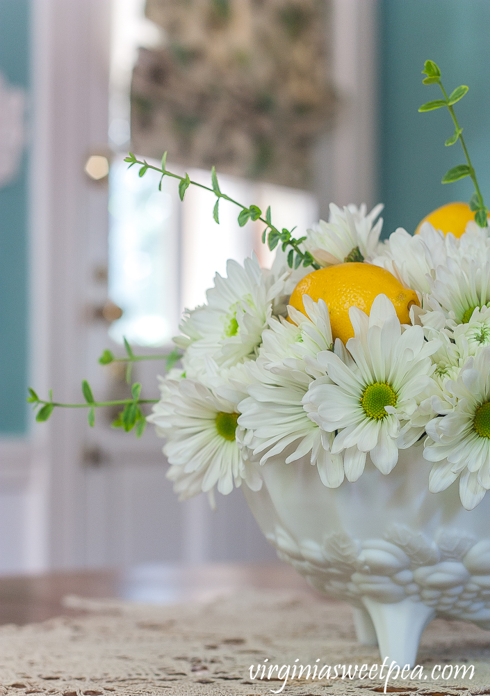 Flower arrangement with Chrysanthemums, and Lemon in a white Indiana milk glass footed fruit bowl.