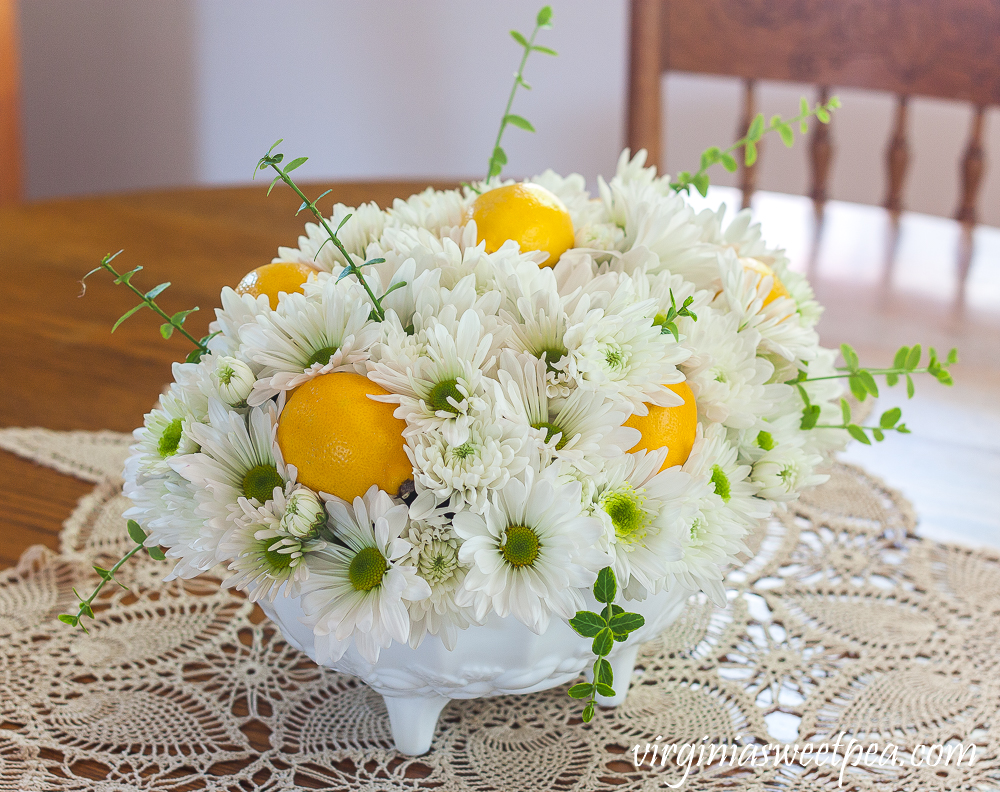 Flower arrangement with Chrysanthemums, and Lemon in a white Indiana milk glass footed fruit bowl.