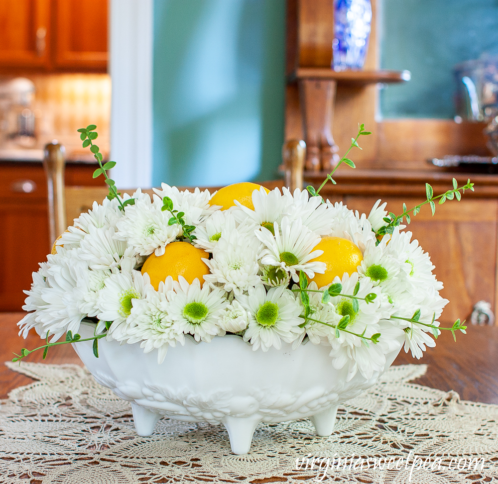 Flower arrangement with Chrysanthemums, and Lemon in a white Indiana milk glass footed fruit bowl.