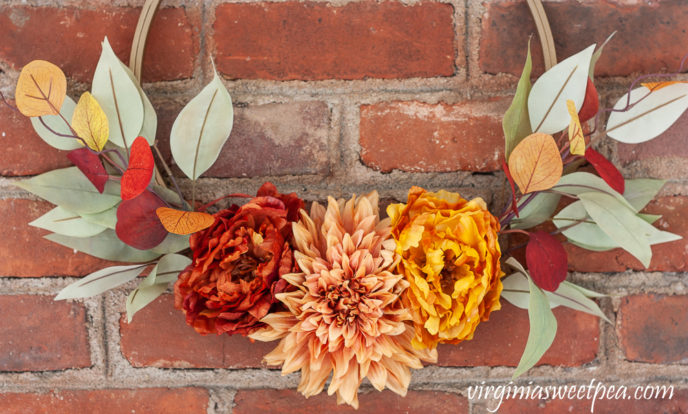 Dark orange, dark blush, and orange faux flowers with greenery on a fall wreath