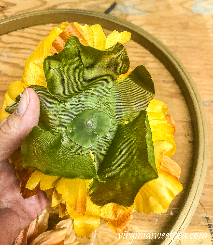 Adding glue to the back of a faux flower to attach it to a fall hoop wreath