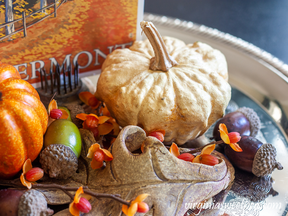 Preserved gourd shaped like a pumpkin on a silver tray with acorns, bittersweet, a pottery leaf, and a Vermont fall postcard