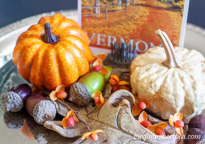 Preserved gourd shaped like a pumpkin on a silver tray with a faux pumpkin, acorns, bittersweet, a pottery leaf, and a Vermont fall postcard