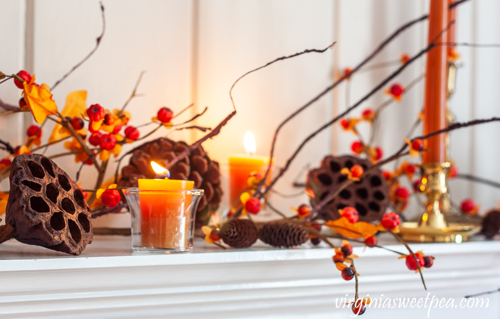 Fall mantel decorated with candles, brass, lotus, pine cones, and bittersweet.