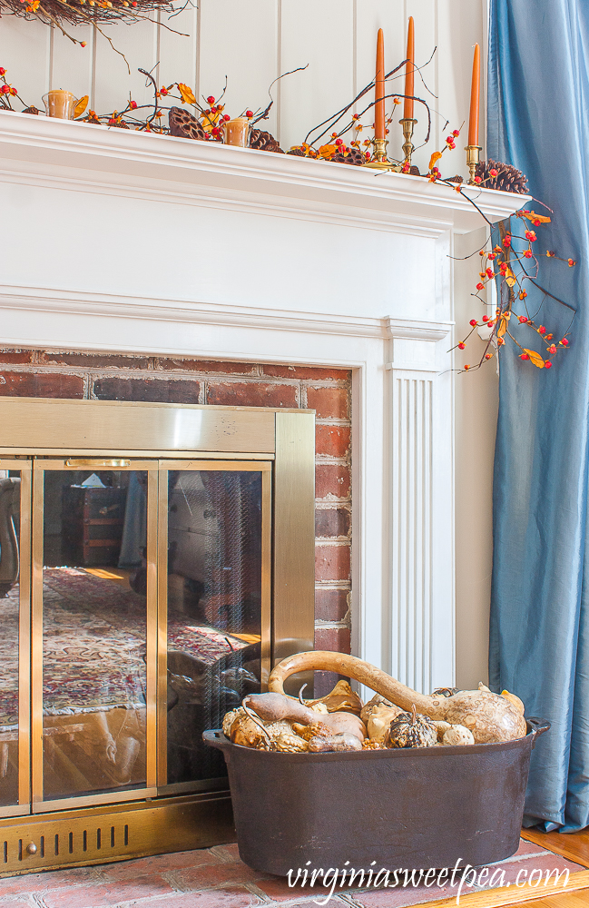 Fall fireplace mantel with dried gourds on the hearth in a black iron tub.